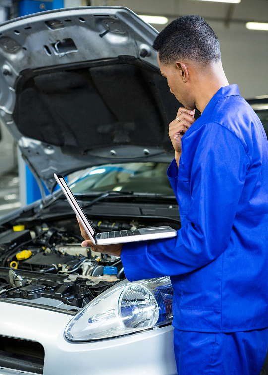 Automotive technician inspecting a vehicle engine with a tablet at Big South Performance